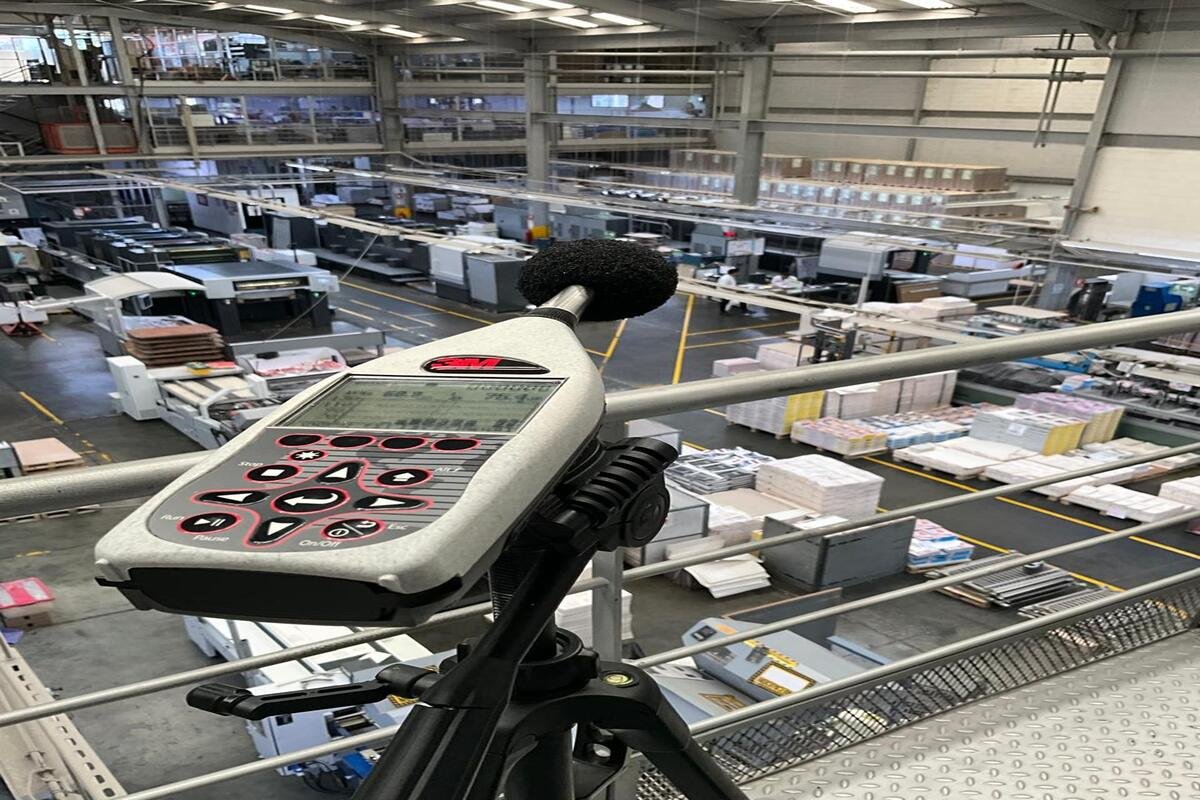 Sonómetro en primer plano midiendo los niveles de ruido ocupacional en una planta de producción industrial para evaluar la exposición de los trabajadores.